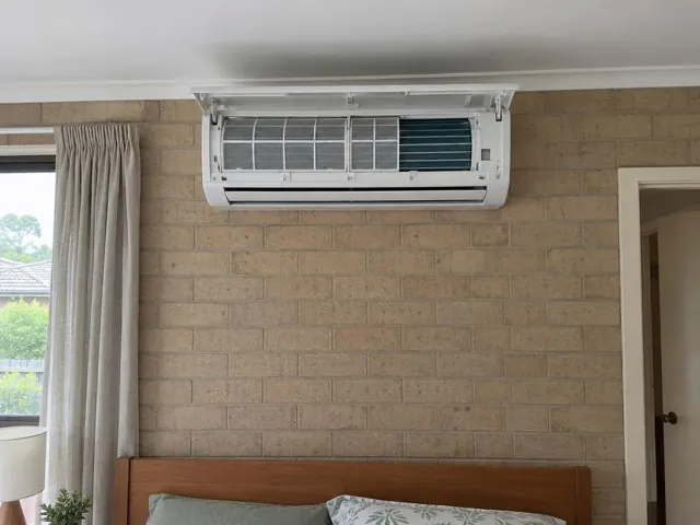 Clean split system mounted high on a brick wall above a bed, with the front panel open and filters visible in Valley View
